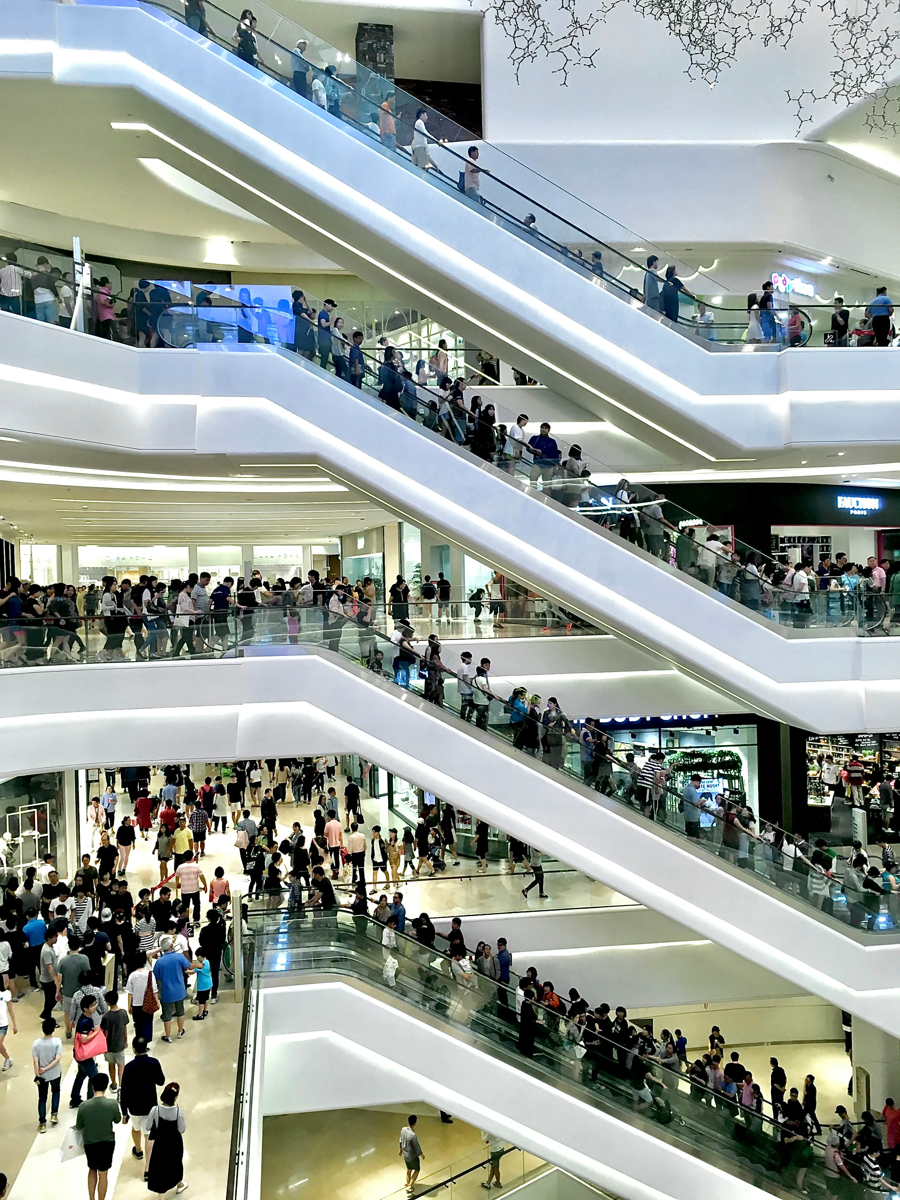 Shoppers riding escalators across several floors of a busy shopping centre
